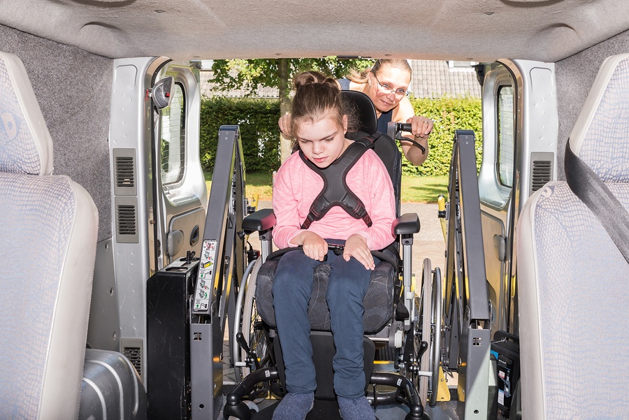 Girl with special needs being helped into a vehicle by a care worker